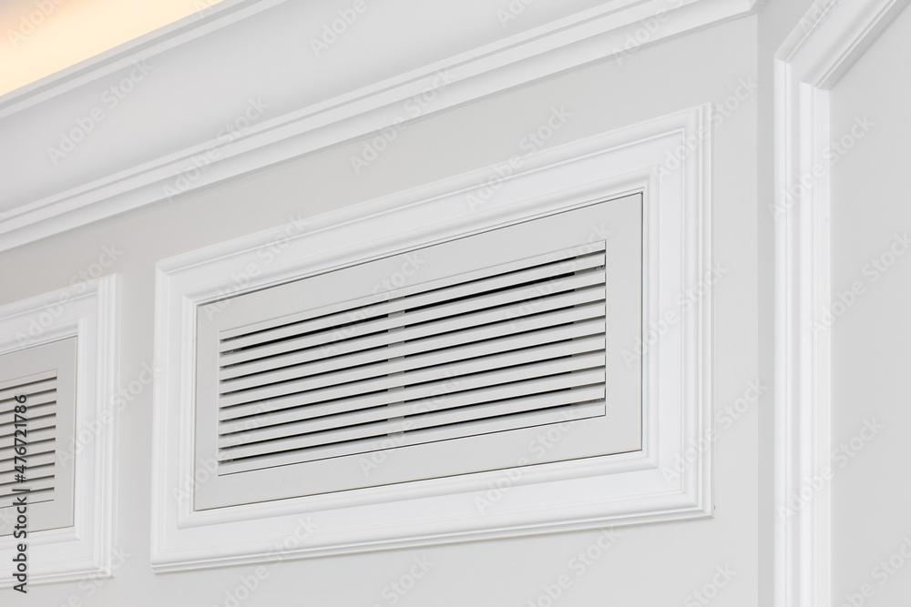 Ventilation grate of conditioning system decorated and disguised with classic white moldings in modern interior. Ventilation grate of conditioning system decorated and disguised with classic white moldings in modern interior.