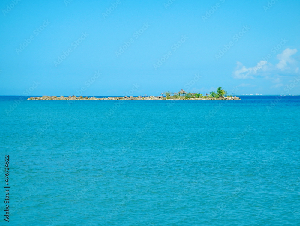 View of a tropical islet with palm trees and a gazebo in Caribbean Sea at summer sunny day