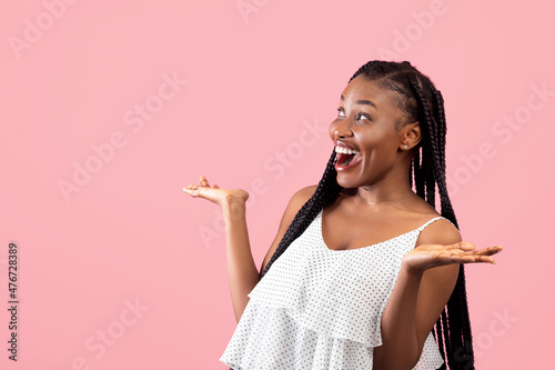 Emotional black lady in summer dress looking at empty space in surprise, screaming OMG on pink studio background