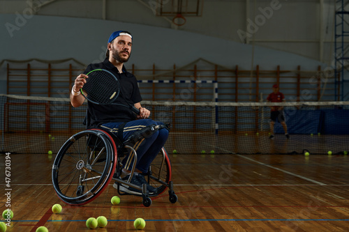Young man in wheelchair playing tennis on court © Georgii