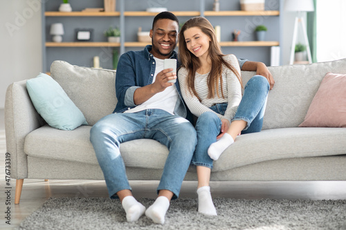 Weekend Pastime. Millennial Interracial Couple Relaxing With Smartphone At Home