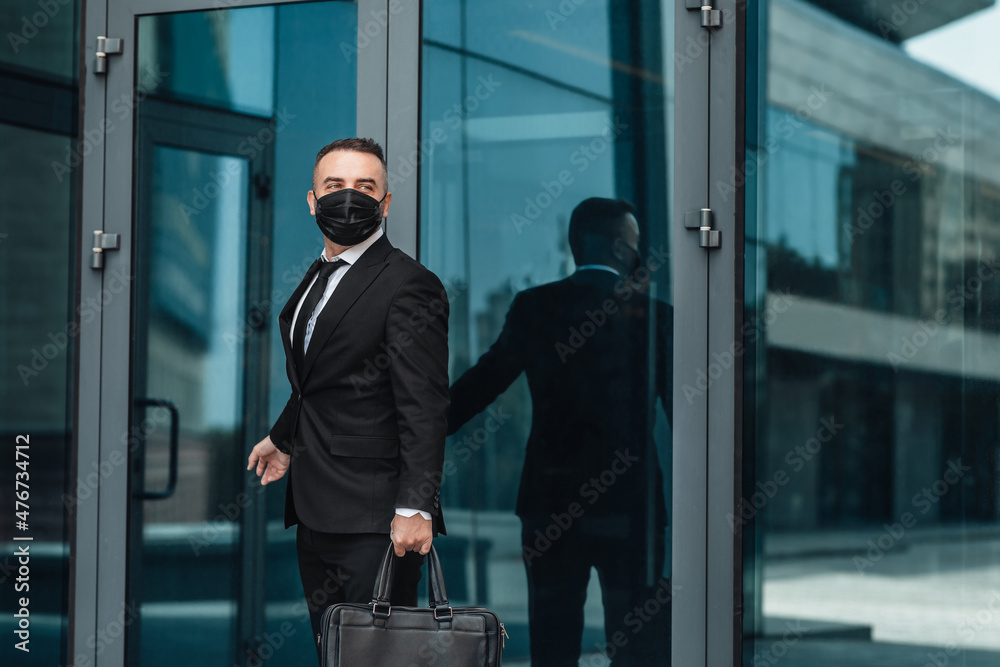 Back to work after covid-19 pandemic. Middle-aged businessman in protective face mask going in modern office building Back to work after covid-19 pandemic. Middle-aged businessman in protective face mask going in modern office building