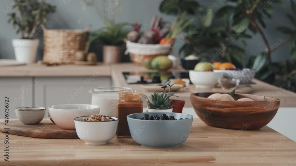 Close up tracking shot of milk and honey in jars and berries, fruit and nuts in bowls standing on kitchen counter Close up tracking shot of milk and honey in jars and berries, fruit and nuts in bowls standing on kitchen counter