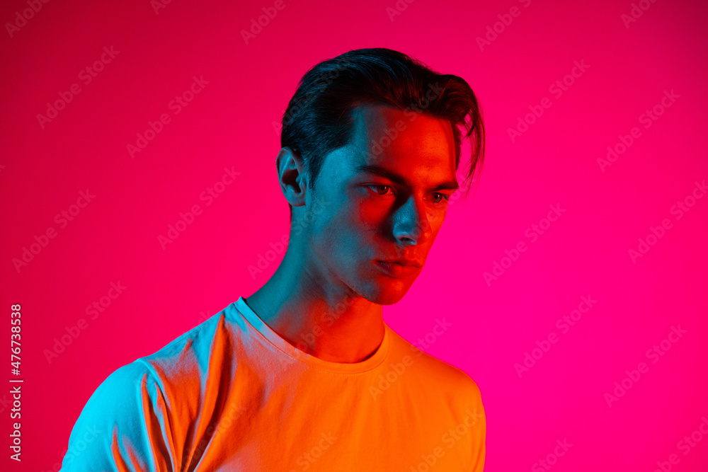 Young serious man posing isolated on magenta studio background in neon light, Concept of human emotions, facial expression