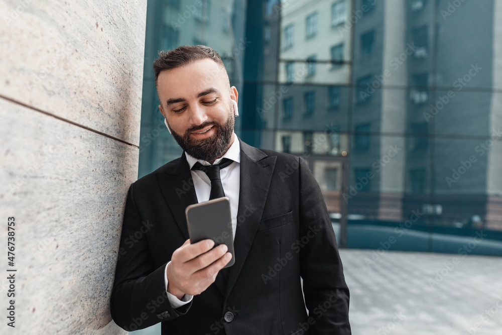 Favorite music during break. Happy entrepreneur in business suit using smartphone and listening music in earphones Favorite music during break. Happy entrepreneur in business suit using smartphone and listening music in earphones