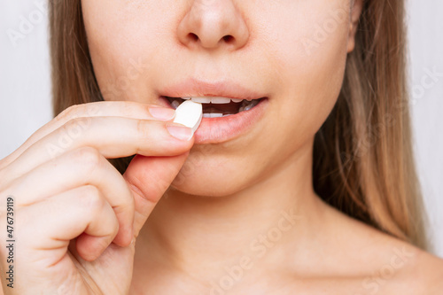 Cropped shot of a young caucasian blonde woman taking a pill. The girl takes medications isolated on a white background. Treatment of the disease. Taking antibiotics