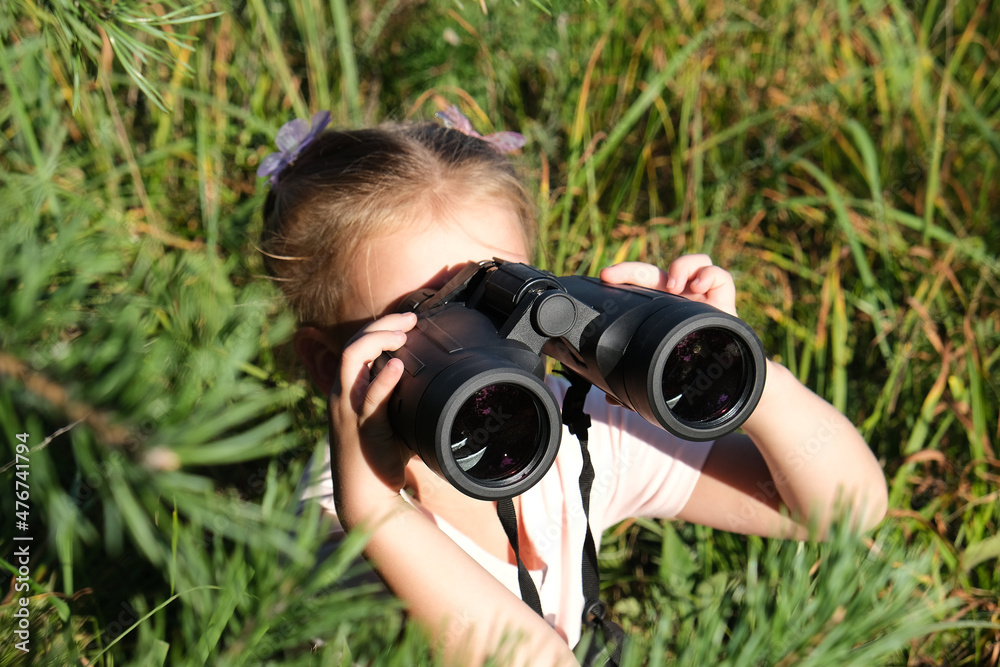 Little girl using binoculars in the forest. Exploring the world. Outdoor activities. Adventure