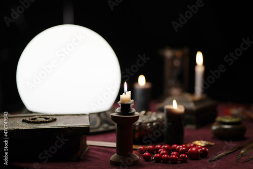 Photo of objects for fortune telling - white crystal ball, candles, book.