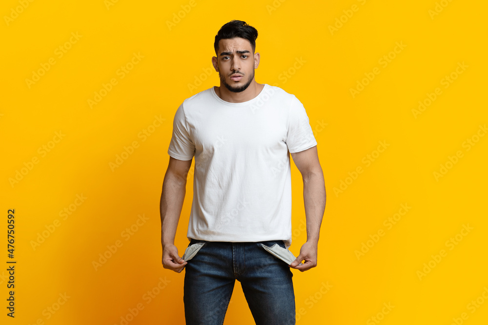 Portrait of sad man showing empty pockets on yellow background Portrait of sad man showing empty pockets on yellow background