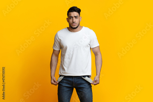 Portrait of sad man showing empty pockets on yellow background