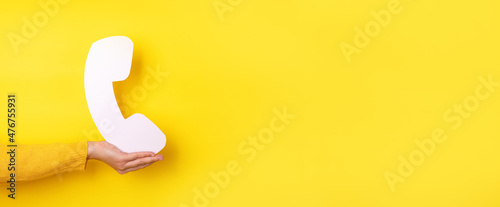 Hand holding symbol of telephone receiver over yellow background, communication concept, panoramic layout