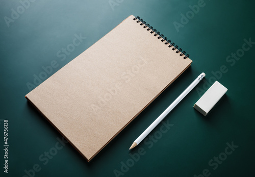 Photo of blank kraft sketchbook, pencil and eraser on green background. Branding identity template.