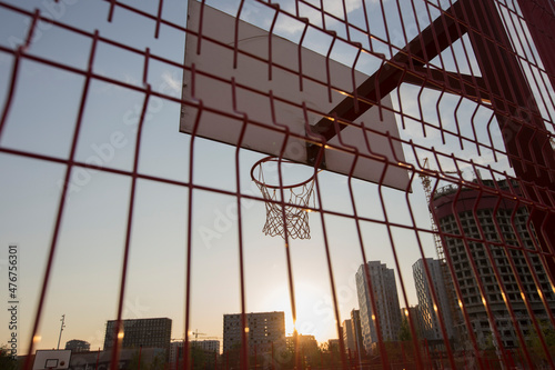 a basketball board with rim and net behind red fence on on buildings background. Tyufeleva Roshcha park, Zilart. !melk landscape architecture urban design