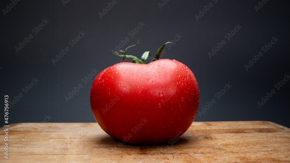 Fresh tomato on the table with splashes of water. On a dark background. Studio shooting, macro photography with dramatic light. Detail shotting. Fresh tomato on the table with splashes of water. On a dark background. Studio shooting, macro photography with dramatic light. Detail shotting.