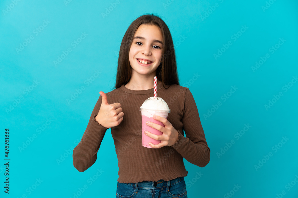 Little girl with strawberry milkshake isolated on blue background giving a thumbs up gesture Little girl with strawberry milkshake isolated on blue background giving a thumbs up gesture