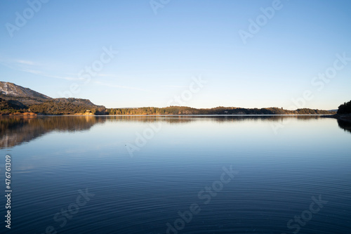 Symmetry in nature. View of the calm lake and shoreline in the horizon. The forest and clear blue sky reflection in the surface of the water. 