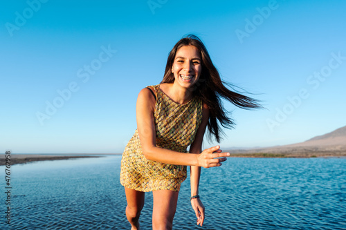 young latin woman smiling with dental braces happy looking at the camera, wide angle close up, outdoor water background