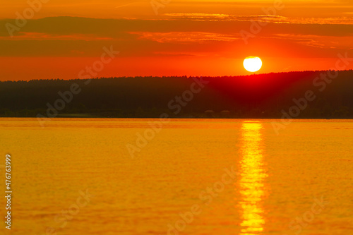 Sunset over the river in summer. Magnificent hot weather contributed to stunning sunsets. The water in the river is completely motionless. Scarlet red sky. Reflected in water of amazing colors.