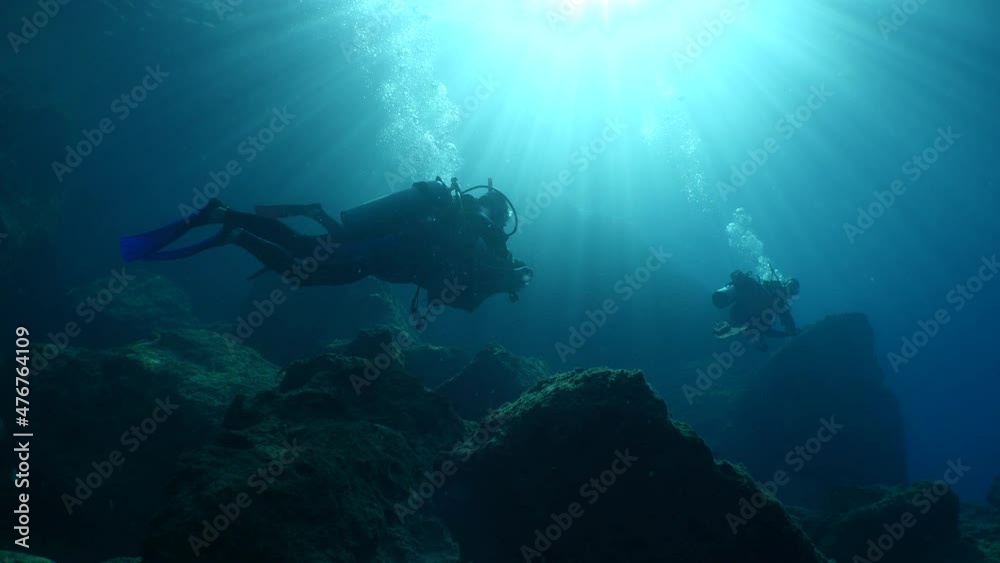 silhouette scuba divers exploring around a reef underwater deep blue water big rocks and bubbles ocean scenery silhouette scuba divers exploring around a reef underwater deep blue water big rocks and bubbles ocean scenery