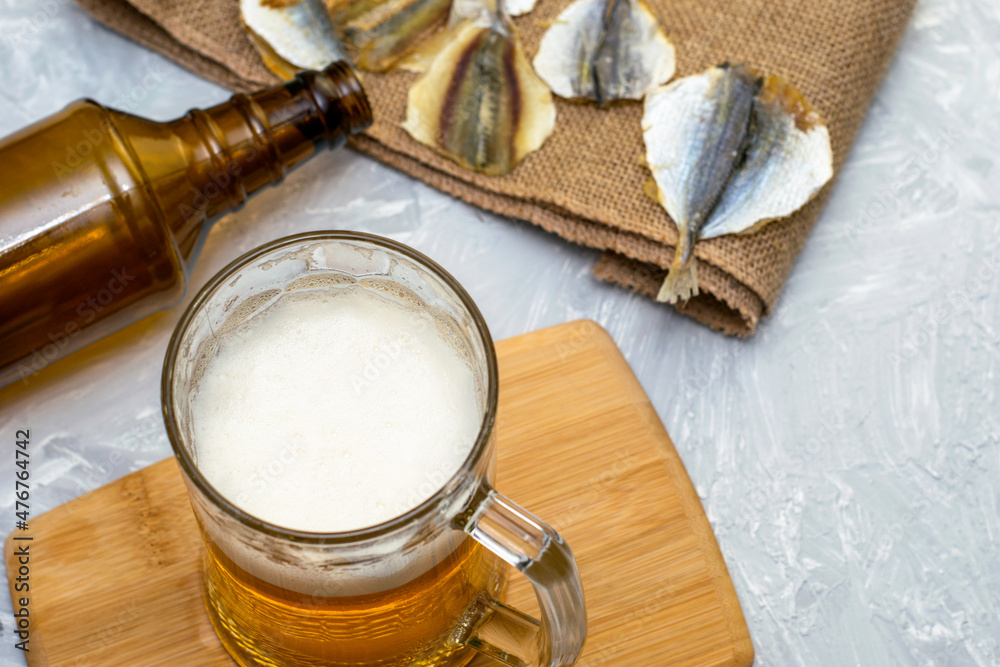 a glass of beer, an empty beer bottle, a cork and dried fish on burlap a glass of beer, an empty beer bottle, a cork and dried fish on burlap