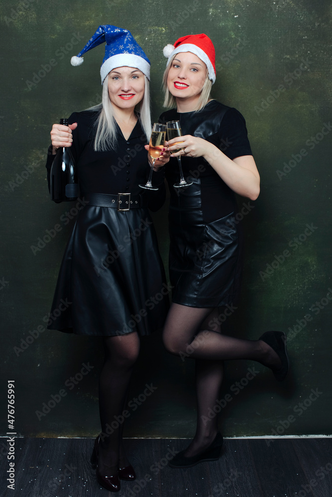 Smiling girls in bright santa hats and black outfits having fun drinking champagne and celebrate the new year. Smiling girls in bright santa hats and black outfits having fun drinking champagne and celebrate the new year.