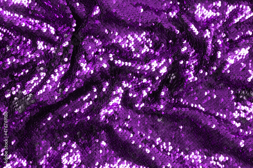 Bright violet sequins background - abstract festive backdrop for Holiday and party banner. Glamour shiny background with sequin texture and blinking lights. Sequins fabric purple color