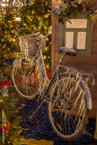 Ice-covered bicycle near cristmas fir-tree and picturesque wooden house in winter Moscow, Russia