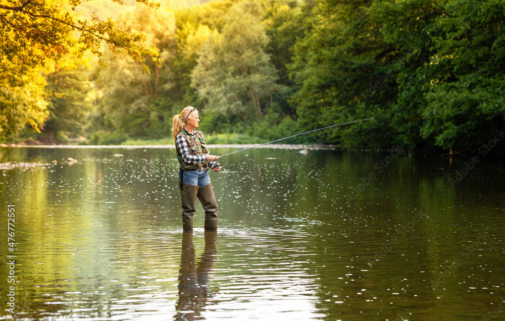 A woman stands in the river and fishes with a spinning rod