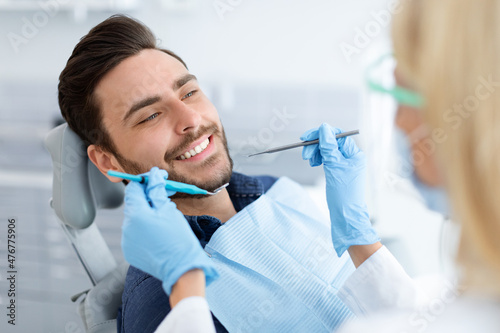 Female dentist in face mask doing treatment for cheerful guy