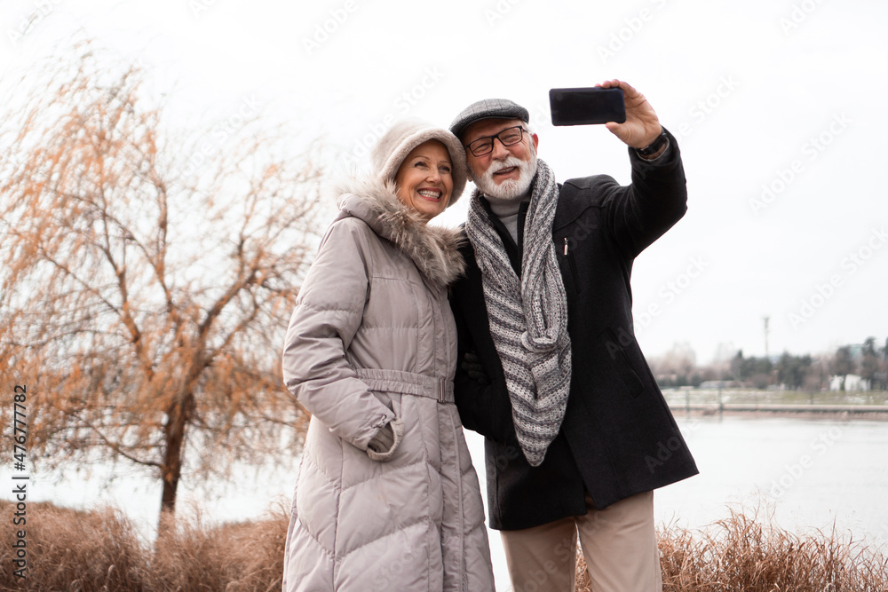 An elderly couple walks around the waterfront in an urban area and takes a selfie. The couple is smiling and looking happy in love. An elderly couple walks around the waterfront in an urban area and takes a selfie. The couple is smiling and looking happy in love.