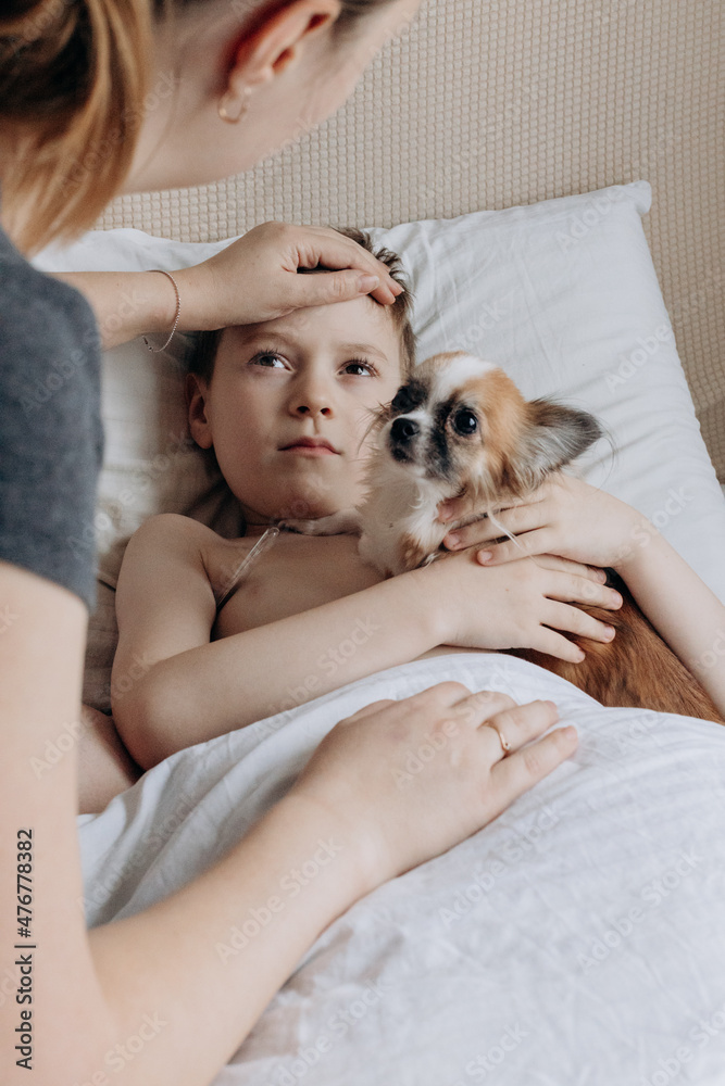 Sick boy with thermometer laying in bed and mother hand taking temperature. Mother checking temperature of her sick son who has thermometer. Sick child with fever and illness in bed. Sick boy with thermometer laying in bed and mother hand taking temperature. Mother checking temperature of her sick son who has thermometer. Sick child with fever and illness in bed.