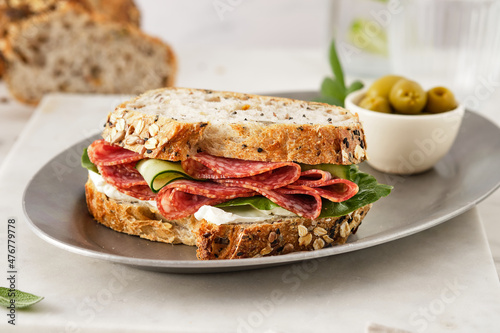 Sandwich with salami sausage and cucumber on marble background.