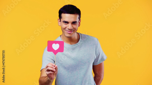 happy young man in t-shirt holding heart on stick isolated on yellow.
