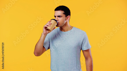 young man in t-shirt drinking coffee to go isolated on yellow.