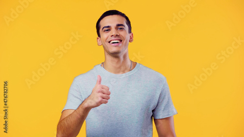 smiling man in t-shirt showing thumb up isolated on yellow.