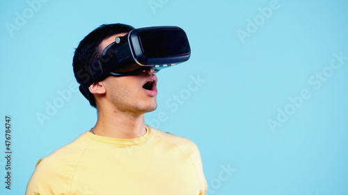 surprised young man gaming in vr headset isolated on blue. © LIGHTFIELD STUDIOS