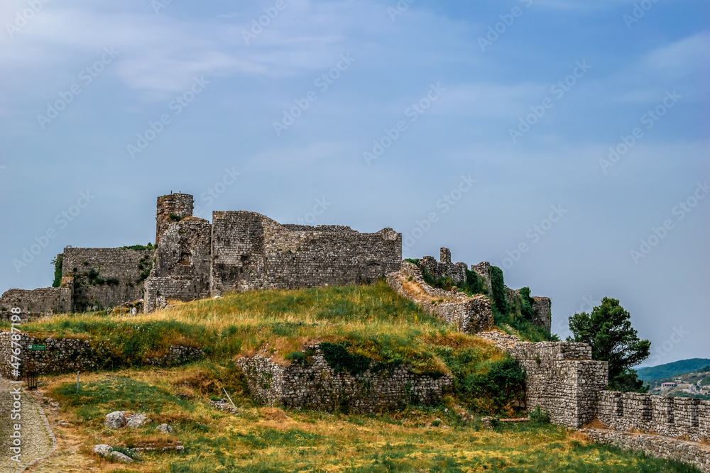 Stone ruins of Shkoder Castle among the green-yellow summer lawn. Remains of a medieval fortress isolated on blue sky background