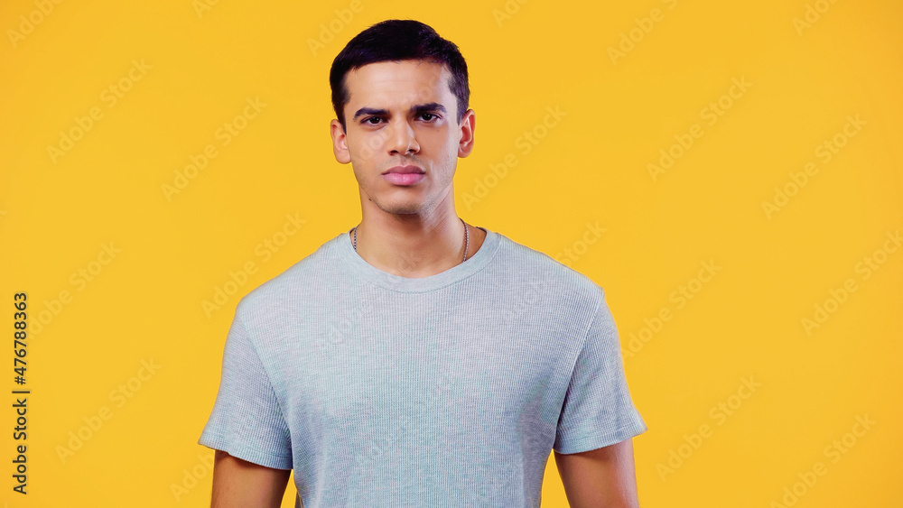 serious young man in t-shirt looking at camera isolated on yellow. serious young man in t-shirt looking at camera isolated on yellow.