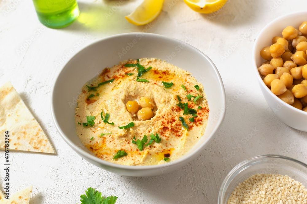 Hummus in a ceramic white bowl with paprika and parsley leaves and ingredients on a light background. A traditional Middle Eastern dish. Horizontal orientation. Healthy nutrition concept. Hummus in a ceramic white bowl with paprika and parsley leaves and ingredients on a light background. A traditional Middle Eastern dish. Horizontal orientation. Healthy nutrition concept.
