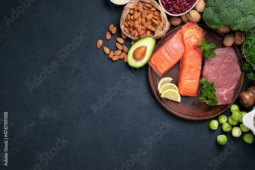 Green vegetables, nuts, beans with beef meat and salmon fish on dark background with copy space top view. Raw healthy food, clean eating or balanced diet concept