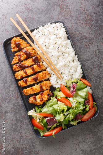 Chicken katsu is a traditional Japanese dish served with rice and vegetables salad closeup in the plate on the table. Vertical top view from above