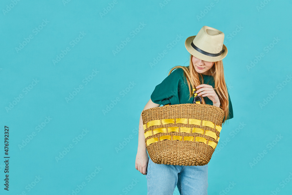 Elegant girl in summer outfit preparing for vacation. Romantic attractive woman in straw hat posing on blue background with bag