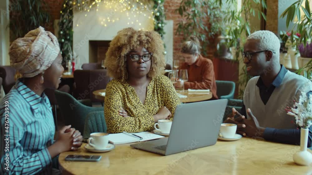 Group of African American colleagues sitting at table in cafe, having coffee and discussing business project on laptop Group of African American colleagues sitting at table in cafe, having coffee and discussing business project on laptop