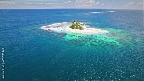 Aerial view of tiny paradise island in the middle of ocean. Island with white sand beach, blue water, palm trees and coral reefs. 