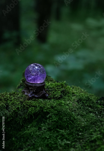Amethyst crystal ball in forest, natural dark green background. Magic quartz ball for healing Crystal Ritual, Witchcraft, spiritual esoteric practice. Reiki life balance concept