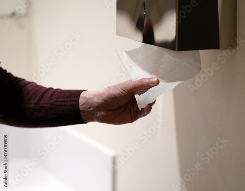 Close-up photo of a hand in a public toilet tearing off paper.
