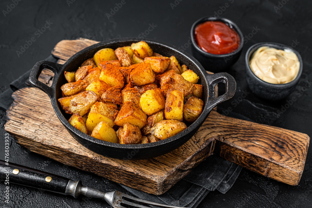 Patatas bravas, spicy potatoes, a Spanish dish with fried potato and a spicy garlic sauce. Black background. Top view