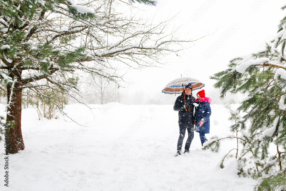 Young man in warm hat and child girl on rural winter snowy background holding umbrella. Happy family, cold weather. Time together. Vacations. Snowy winter, lost in forest. Outside