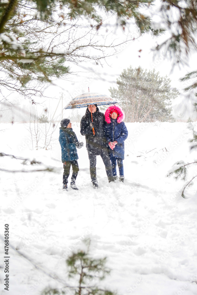 Young man in warm hat and children girl and boy on rural winter snowy background holding umbrella. Happy family, cold weather. Time together. Vacations. Snowy winter, lost in forest. Father and kids