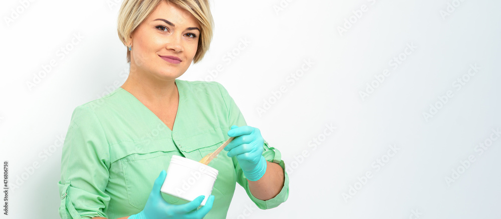 Cosmetician holding a jar of wax for depilation smiling on a white background. Natural product for hair removal. Copy space Cosmetician holding a jar of wax for depilation smiling on a white background. Natural product for hair removal. Copy space